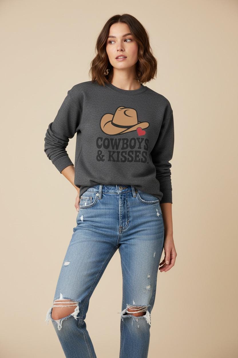 Model wearing a charcoal Cowboys & Kisses sweatshirt featuring a cowboy hat and heart graphic.