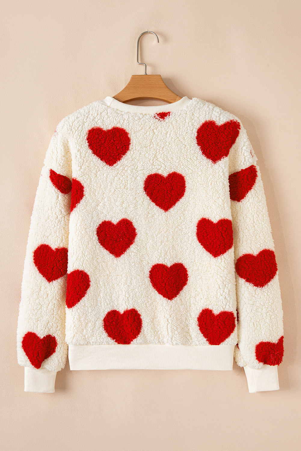 Cream sherpa sweatshirt with red heart shapes, drop-shoulder crewneck, plush cozy fabric.
