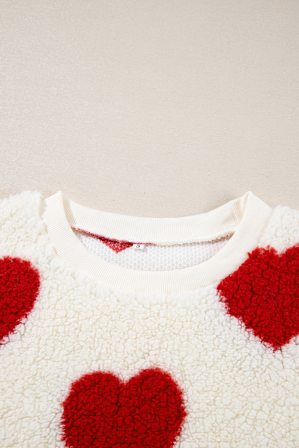 Close-up of white plush sherpa sweatshirt with bold red heart shapes and ribbed crewneck.